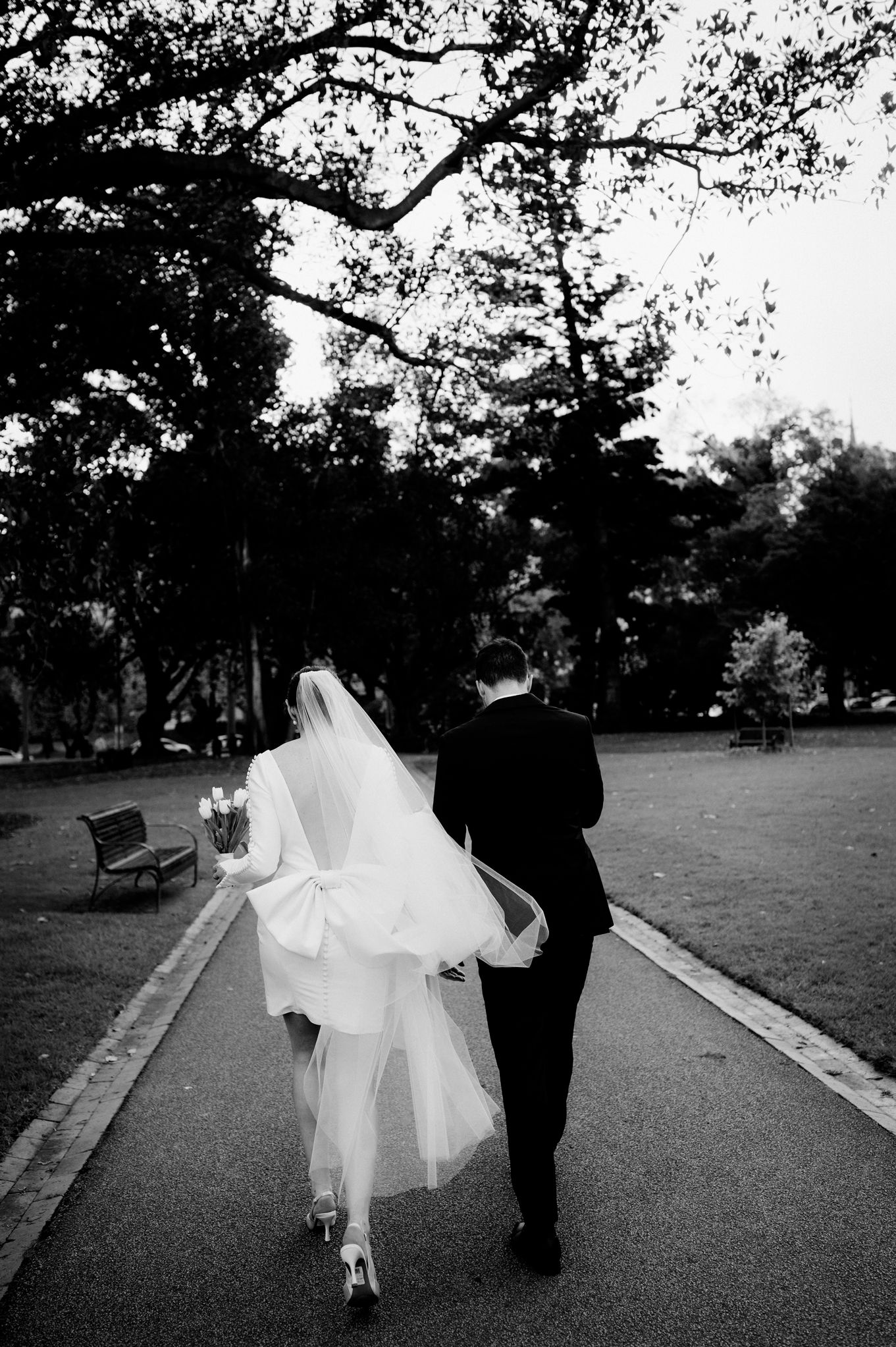 A wedding couple walks along a park path in black and white photography.