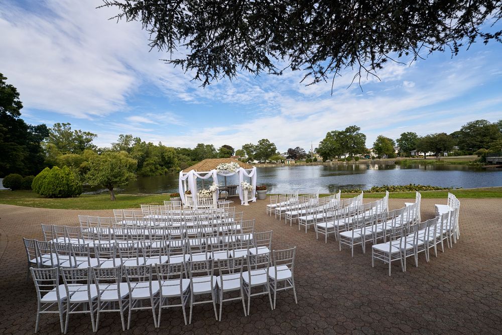 White chairs arranged for an outdoor wedding ceremony next to a scenic lake under blue skies.