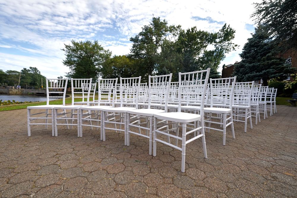 Rows of white Chiavari chairs set up for an outdoor ceremony.