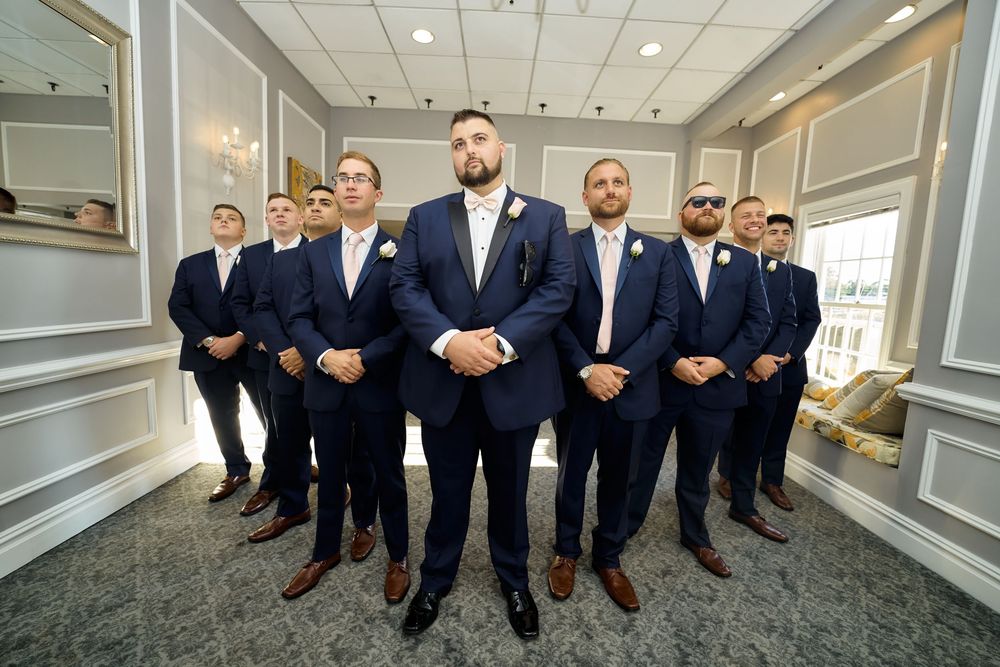 Formal group standing in v-formation in an elegant hallway with paneled walls.