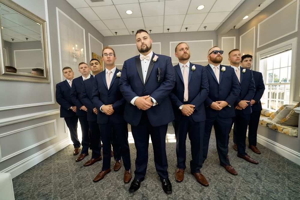 Wedding party in navy suits and brown shoes standing in formation.