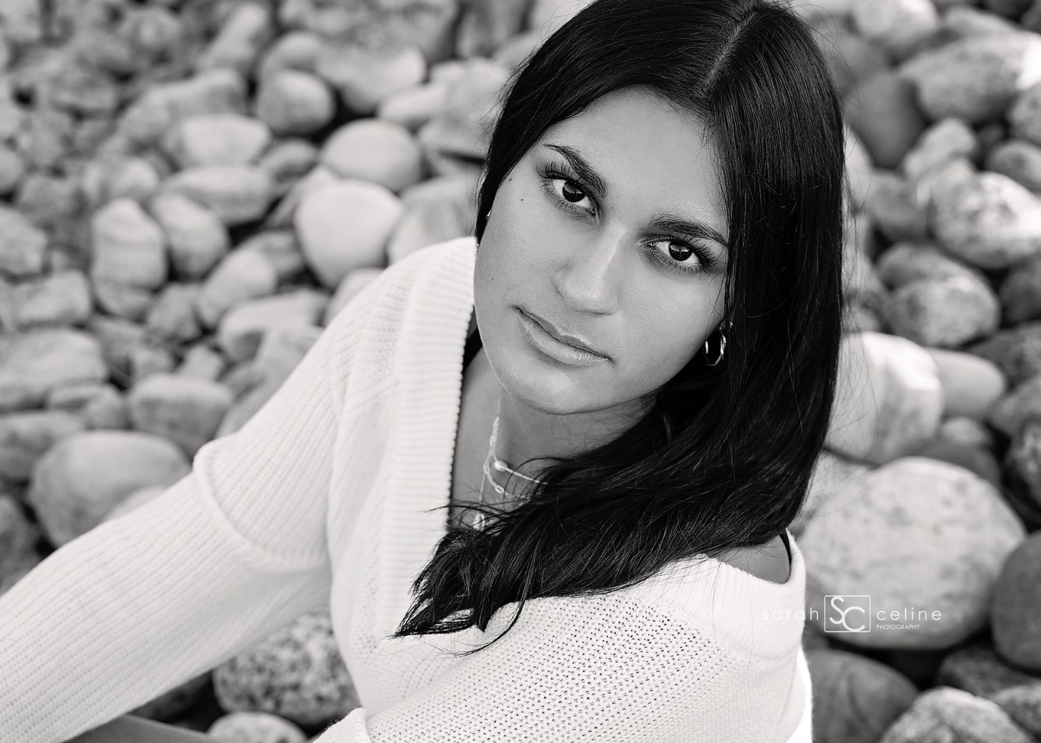 Young person in white sweater looking at camera against decorative stone background.