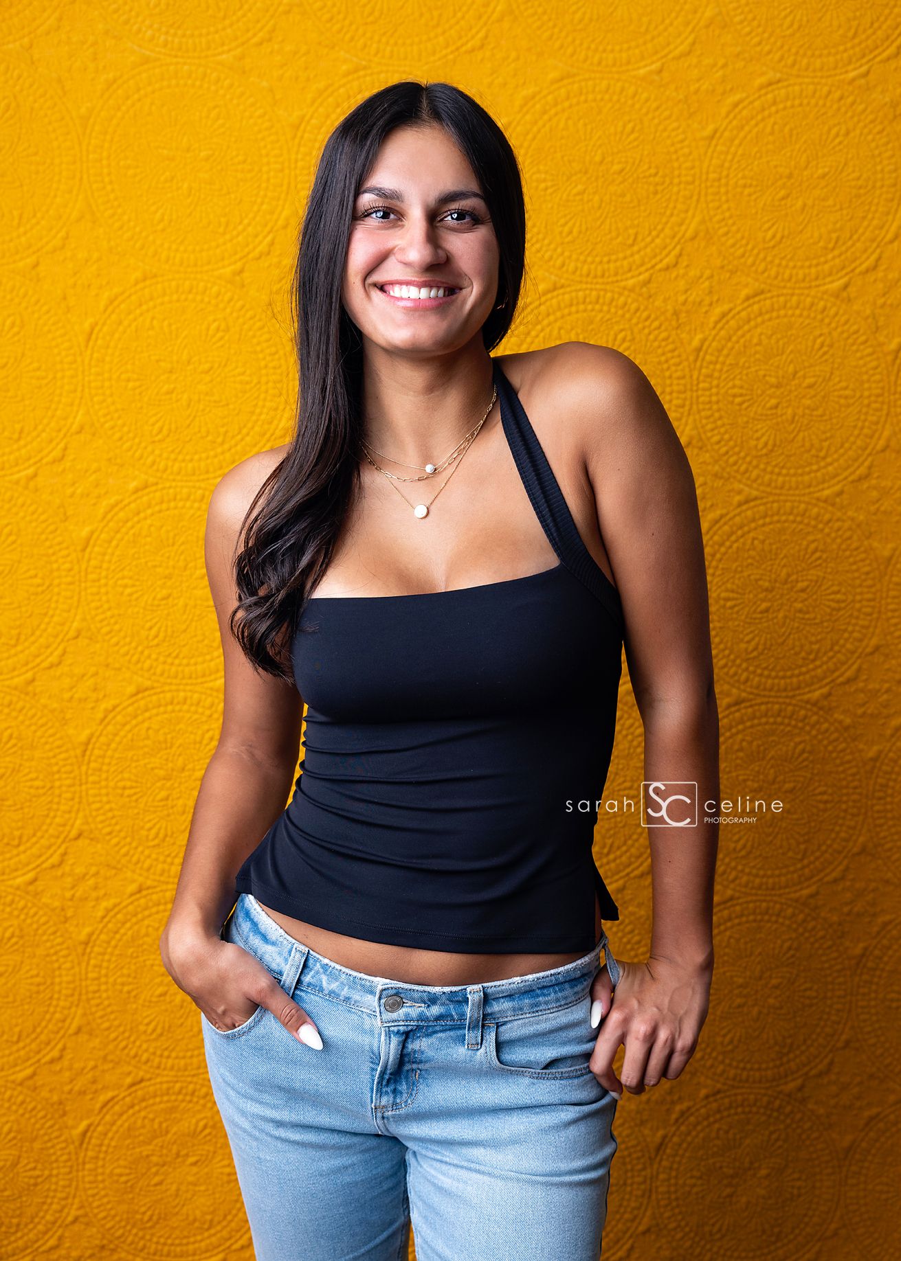 Woman in black tank top and light blue jeans poses against vibrant yellow wall in four similar fashion shots.