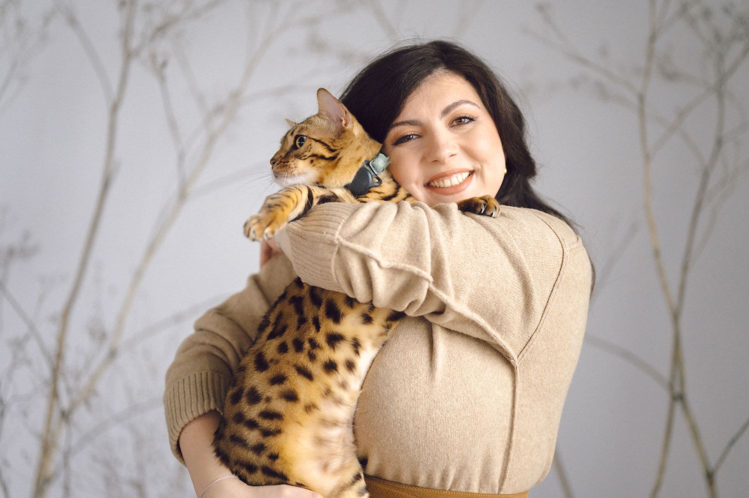 A Bengal cat with distinctive spotted markings is held lovingly in a warm embrace against a light-colored background.