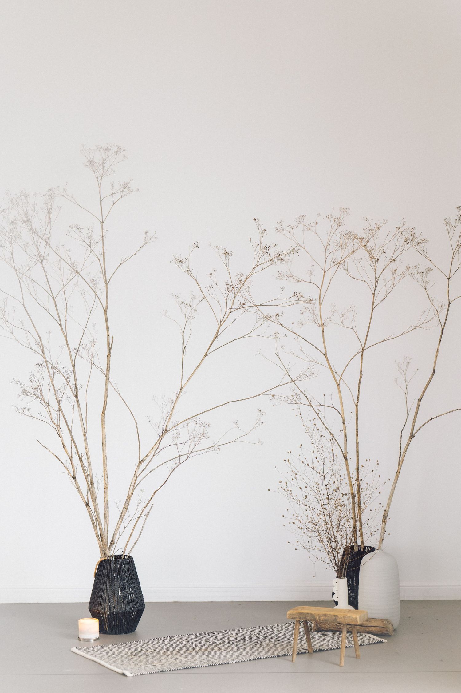 Minimalist decor arrangement with dried branches in geometric black and white vases against a plain wall.