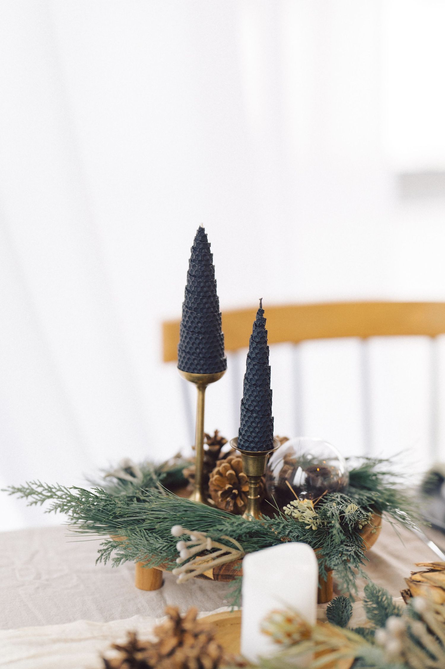Elegant Christmas centerpiece with dark pine cones, evergreen sprigs and pinecones arranged on a white surface.