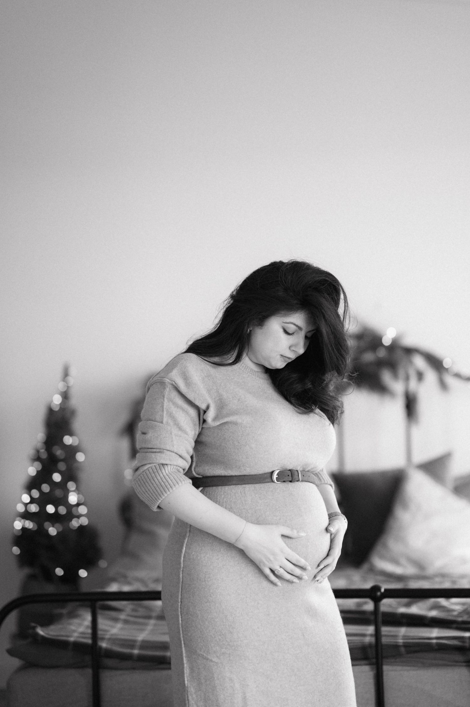 Black and white maternity photos showing pregnant woman cradling belly near Christmas tree.