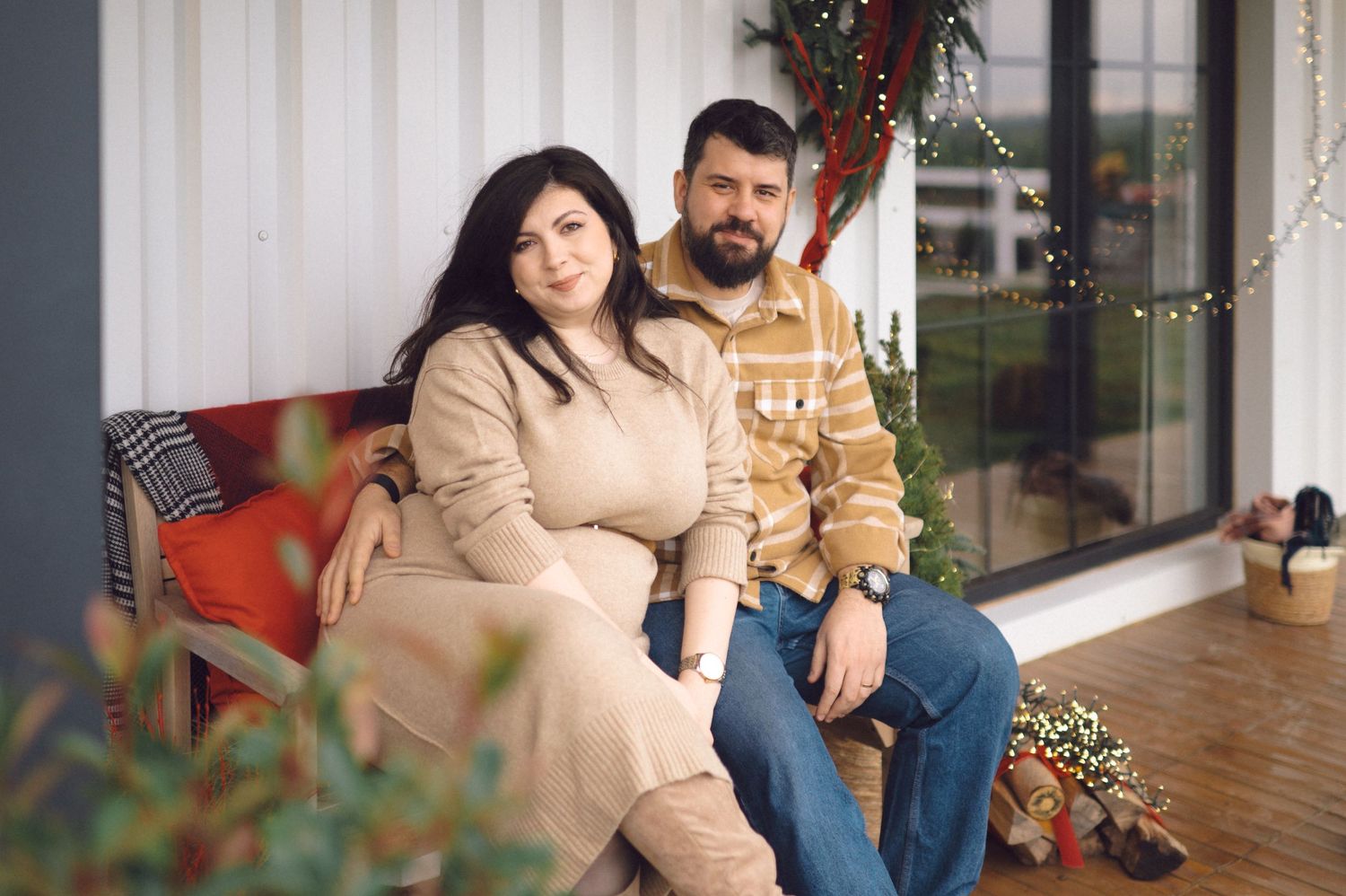 Couple sitting together on rustic wooden steps with autumn foliage decorations and pumpkins.