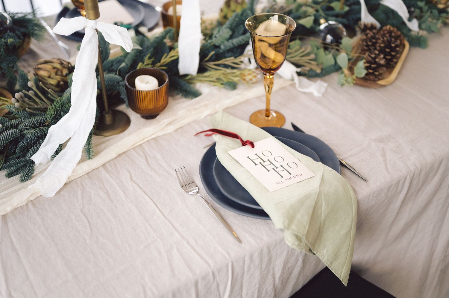Elegant wedding reception table with delicate greenery garland, white candles, and gold accents on neutral tablecloth.