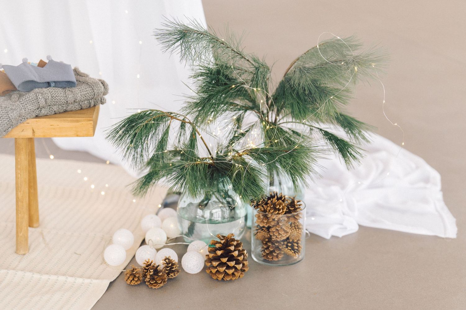 Snowy winter scene with pine branches, pinecones and white decorative ribbon arranged against a beige background.