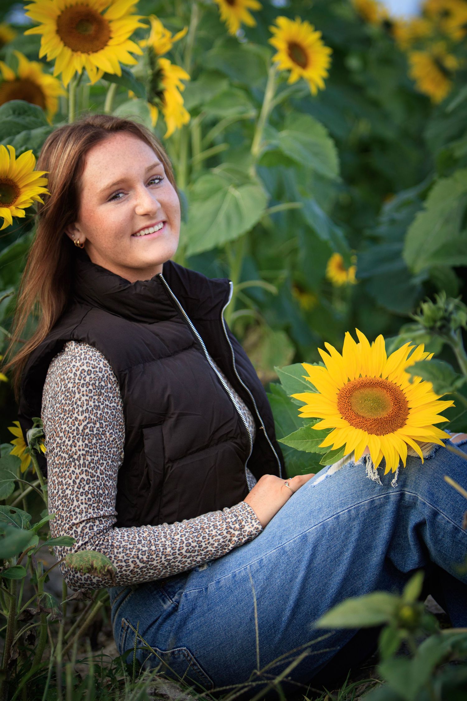 Young woman in white halter top and denim shorts sitting on grass outdoors, smiling warmly at camera.