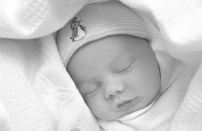 Peaceful sleeping newborn baby wearing white hat with bunny embroidery in soft blanket.