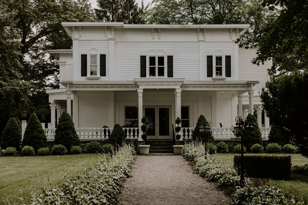 Elegant white colonial wedding venue with manicured hedges and a tree-lined gravel pathway.