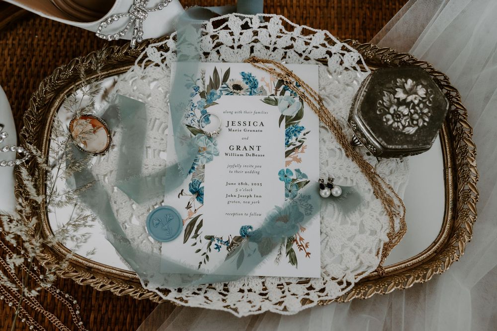 Wedding invitation suite for Jessica and Grant displayed on a decorative tray with blue ribbon and accessories.