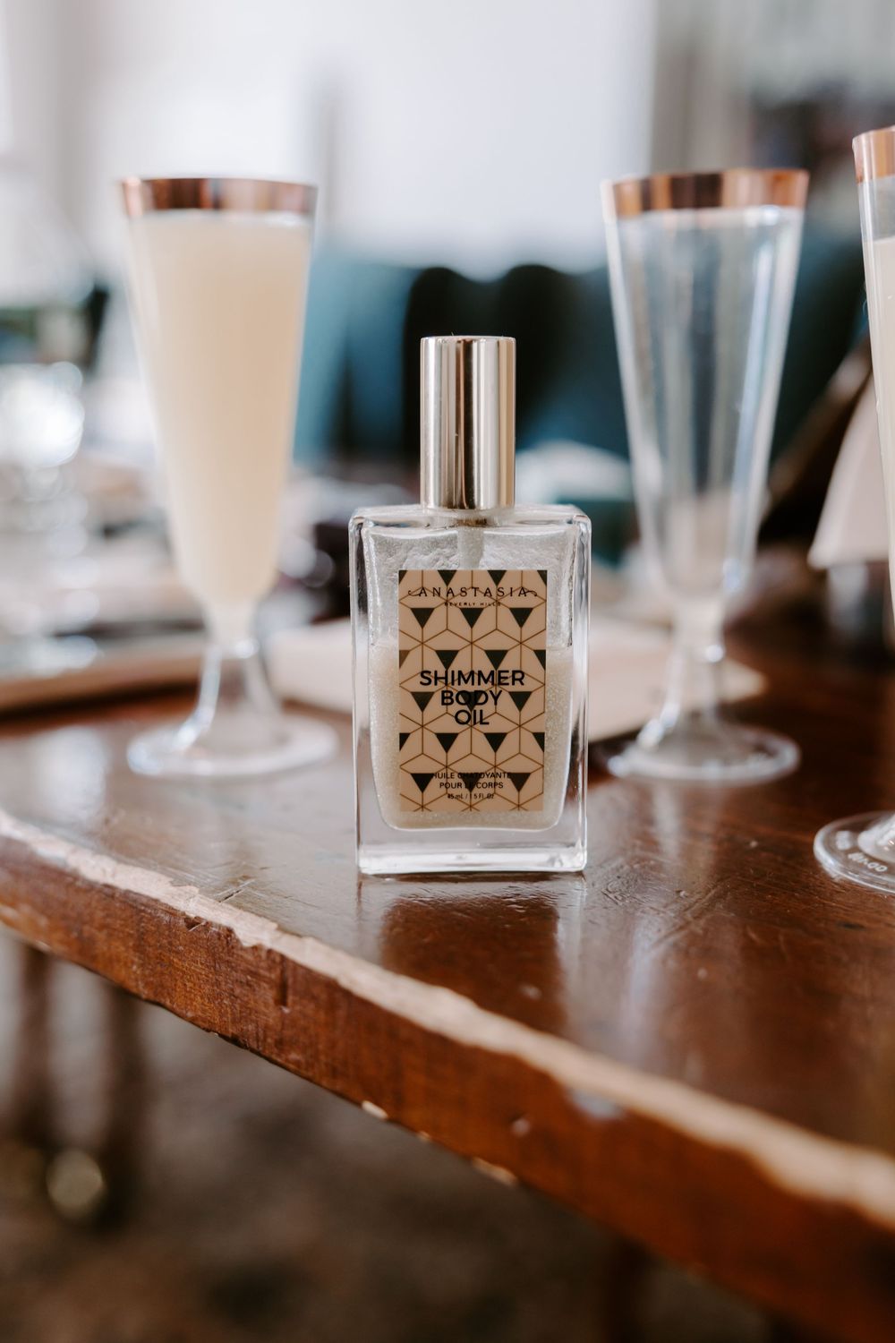Shimmer body oil bottle displayed on a wooden tray with champagne flutes in the background.