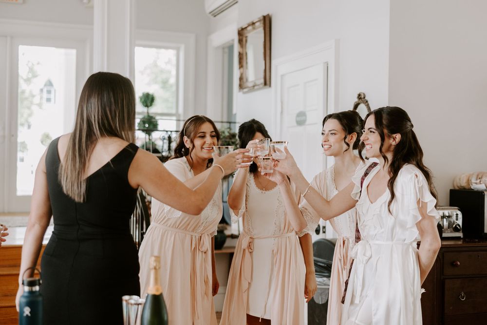 Bridesmaids in pink robes toasting champagne glasses indoors before wedding.