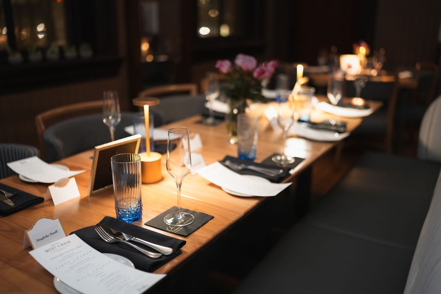 Elegant restaurant table set for dinner with candles, wine glasses, and floral centerpieces in a dimly lit dining room.