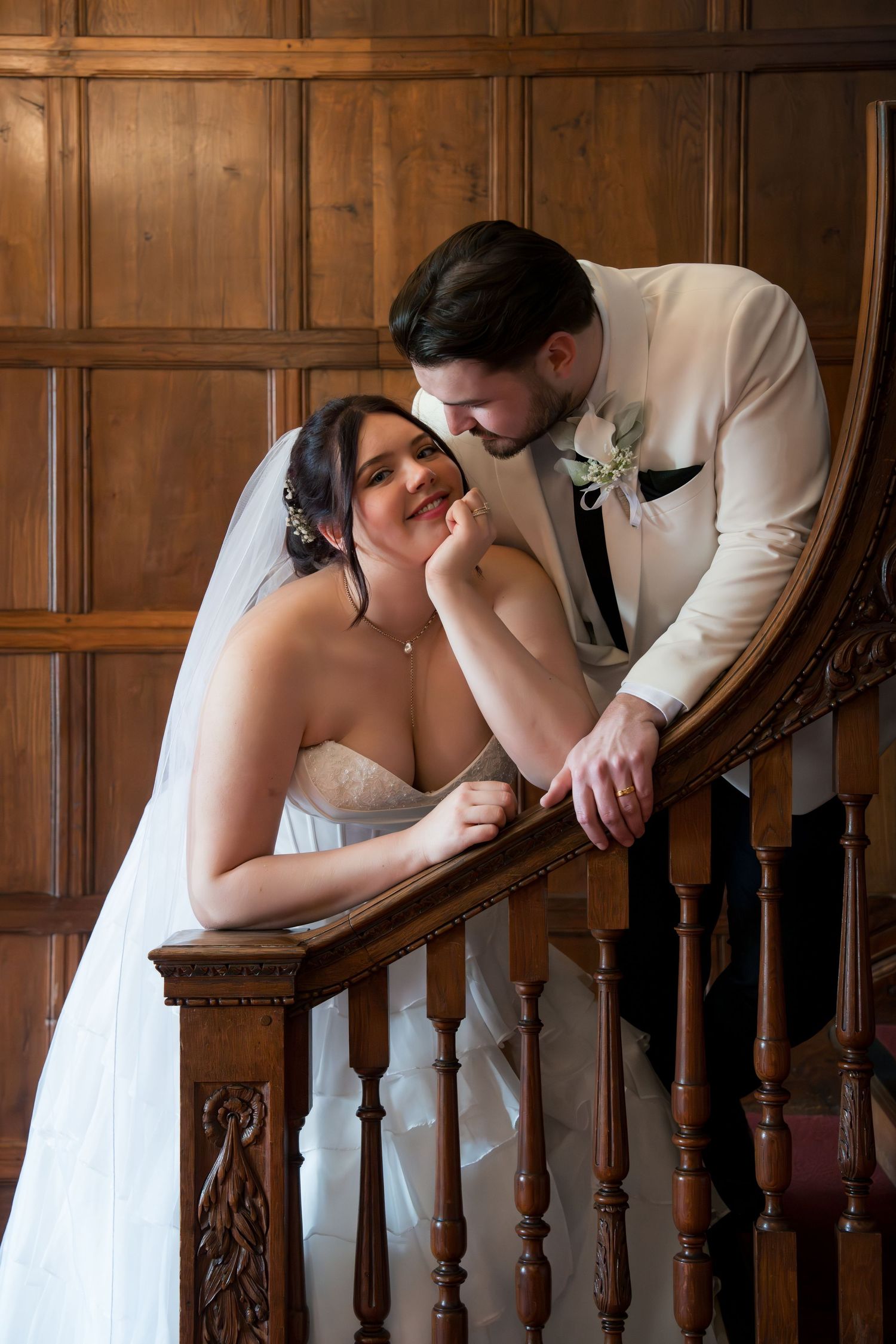 Bride and groom share romantic moment under flowing wedding veil outdoors in lush green garden setting.