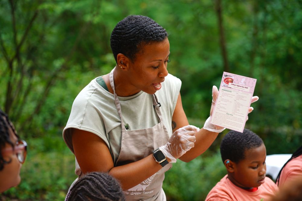 A healthcare worker in gloves reviews a medical document outdoors near a child in a wooded setting.