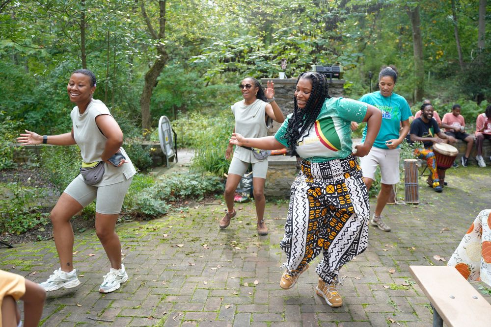 Group of people dancing energetically outdoors at a wellness retreat in a lush green setting.