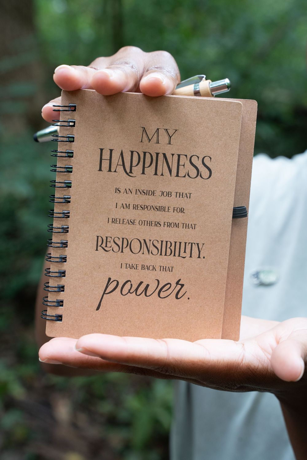 Hands holding a spiral notebook with an inspirational quote about happiness and responsibility.