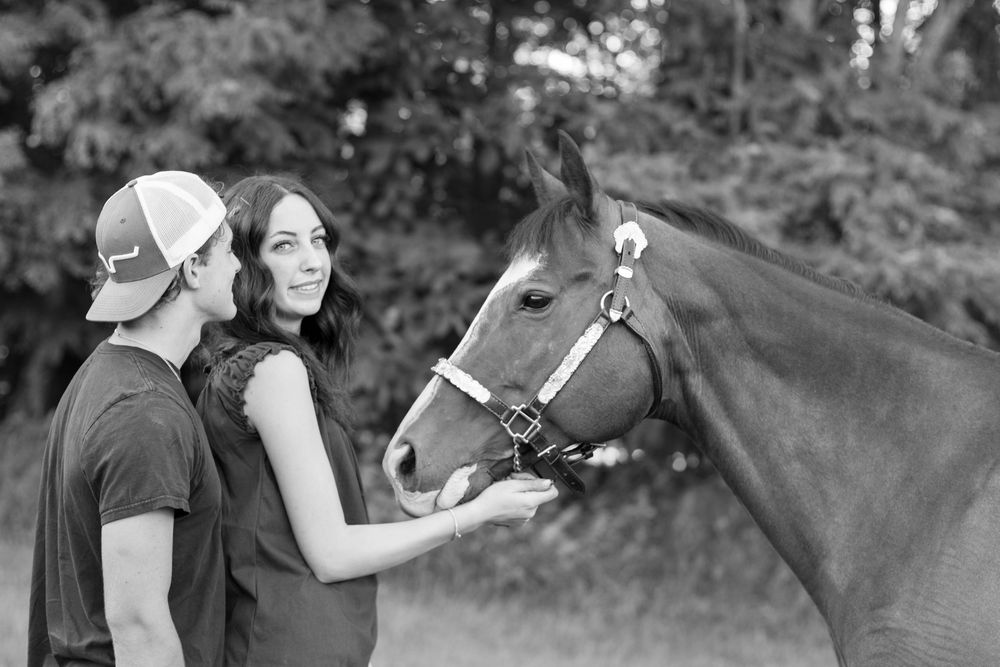 Black and white photo of a couple petting a horse outdoors near trees.