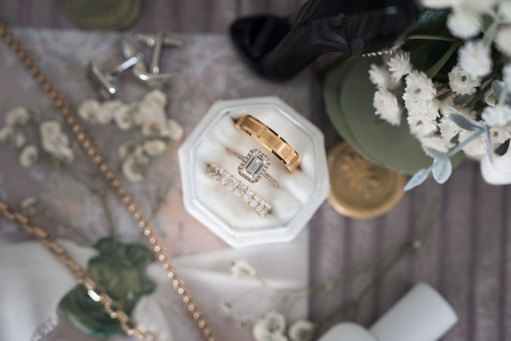 Elegant wedding ring displayed with delicate white flowers and pearls on a soft gray background.
