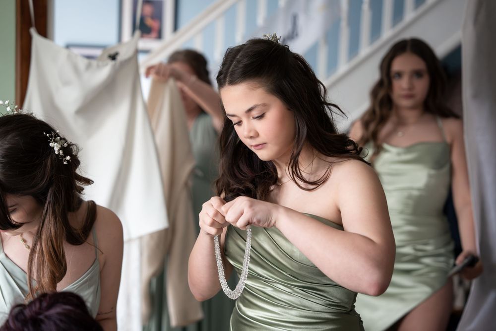 Bridesmaids in sage green dresses prepare for a wedding ceremony.