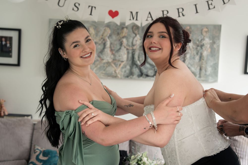 Two people in pastel dresses share a joyful moment at a wedding celebration with 'Just Married' text visible above.