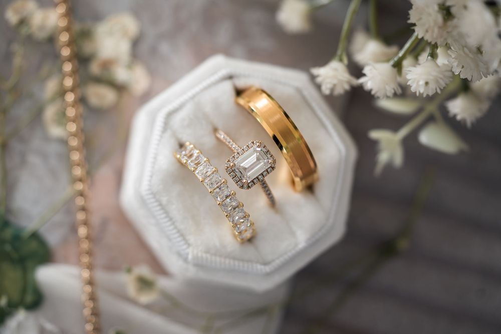 Close-up view of delicate wedding rings and jewelry displayed on white ceramic ring holders with floral accents.