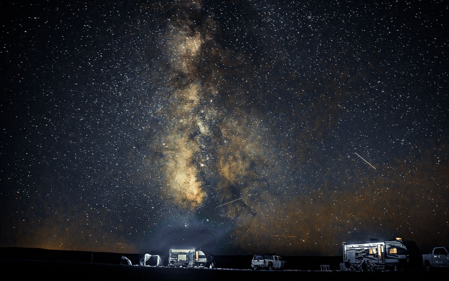 RVs parked under a stunning Milky Way galaxy night sky filled with stars in a remote dark sky location.