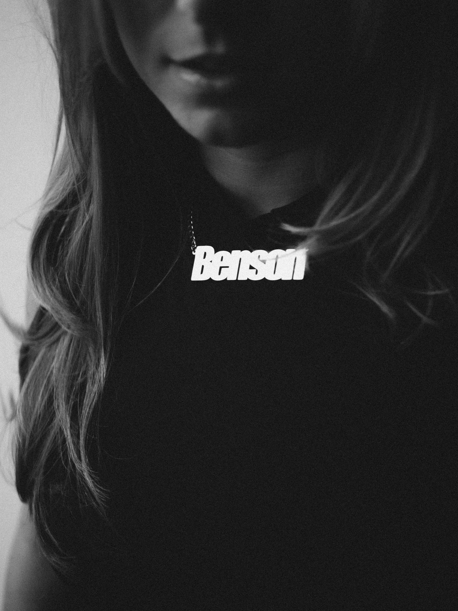 Black and white photo of a woman wearing a Benson name necklace over a black top.