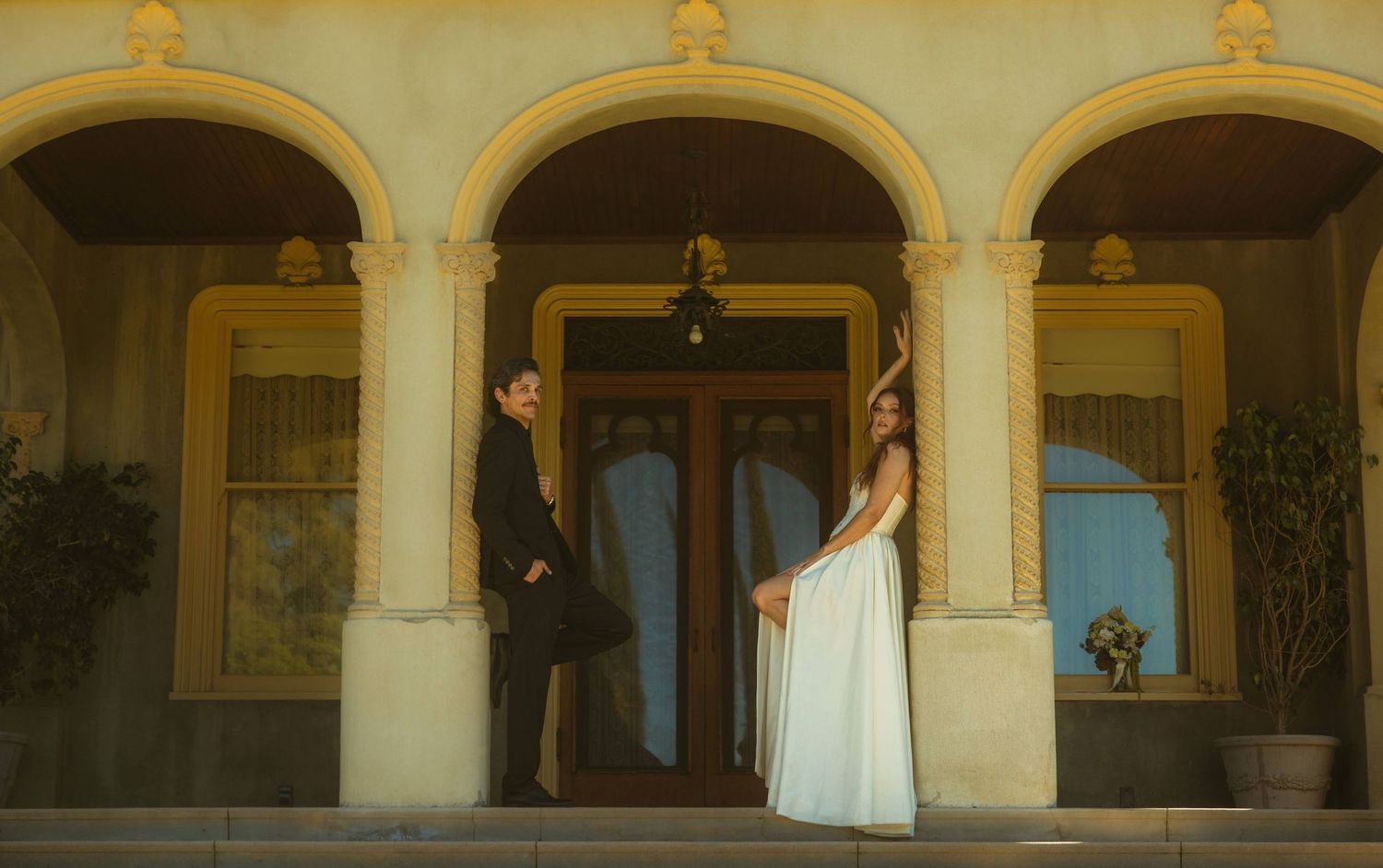 Elegant couple in formal attire standing on ornate building entrance with arched columns at the Kimberly Crest House wedding venue.