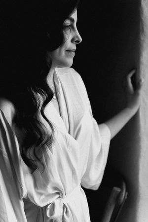 Black and white portrait of a woman in a white robe with long wavy hair, gazing downward in soft light.