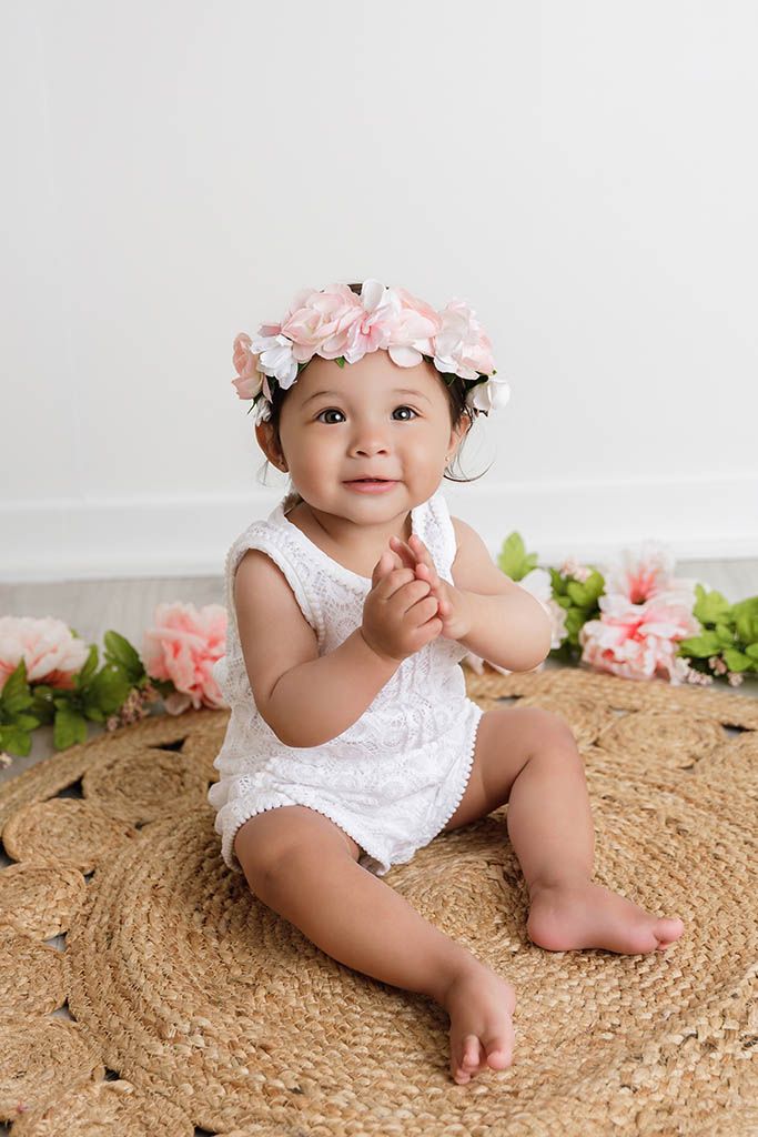 Adorable baby girl in white lace romper and floral crown by Perris baby photographer.
