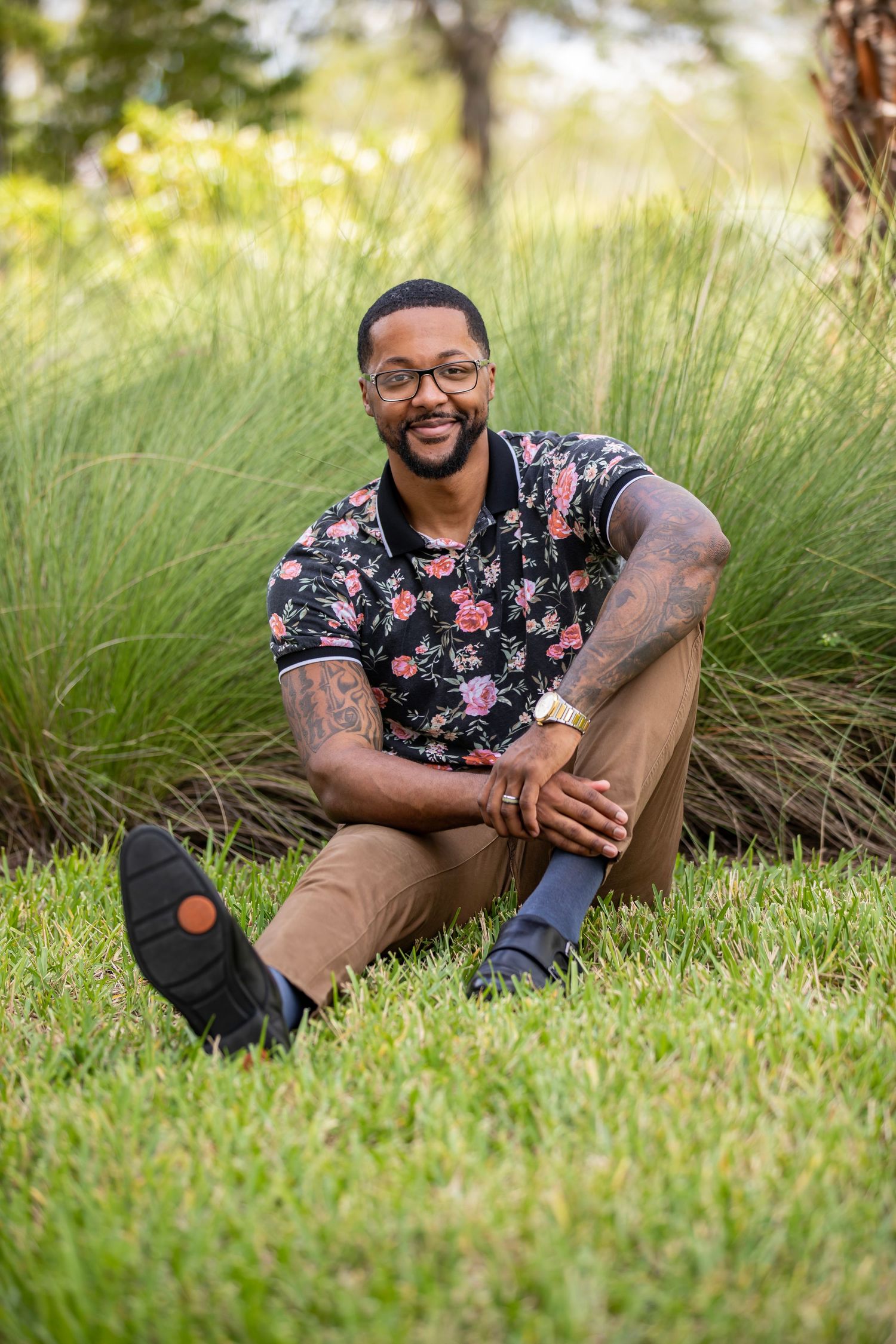 Casual portrait session of person in floral shirt sitting on grass with natural lighting.