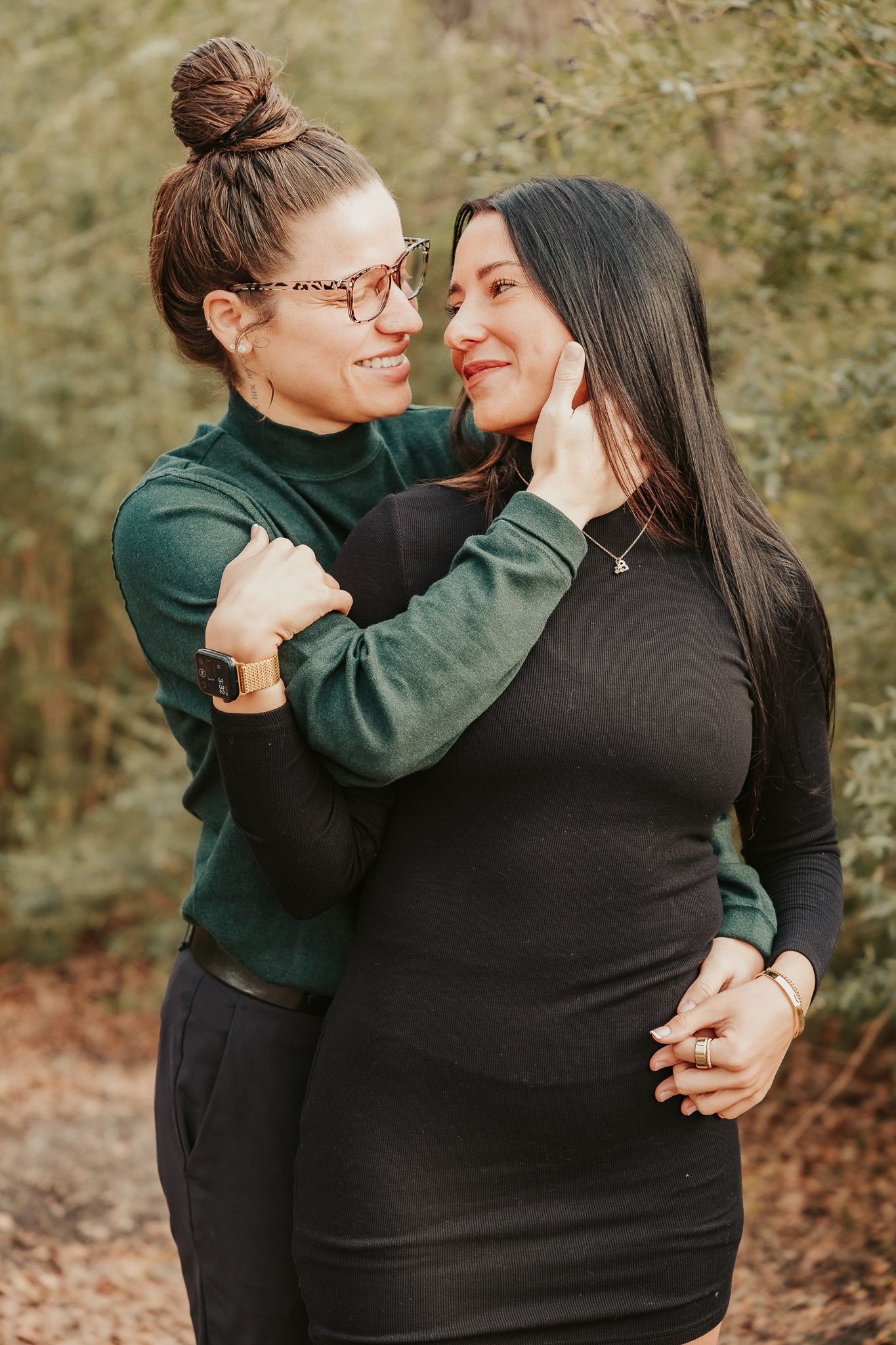 Two women share a tender moment outdoors, one pregnant, embracing and gazing at each other lovingly.