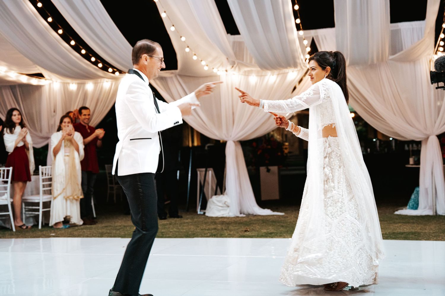 Bride and groom share first dance at elegant wedding reception with white draping and string lights.