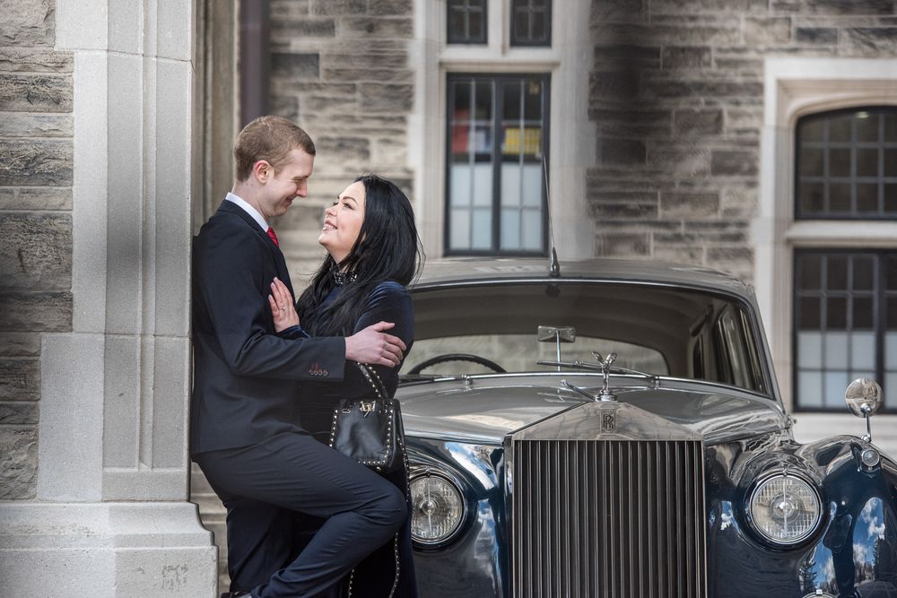 Couple sharing a romantic moment leaning against a vintage Rolls-Royce outside a stone building.