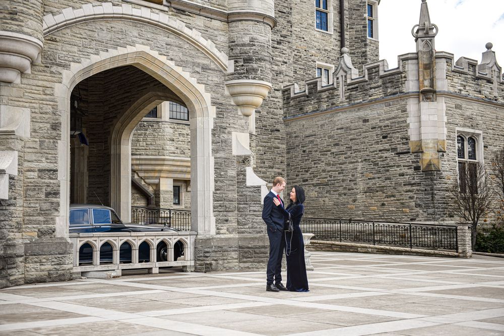 Couple embracing beside the ornate stone archway entrance of a historic castle.