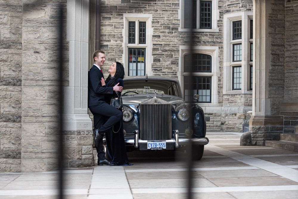 Bride and groom posing beside a classic vintage Rolls-Royce in front of a historic stone building.