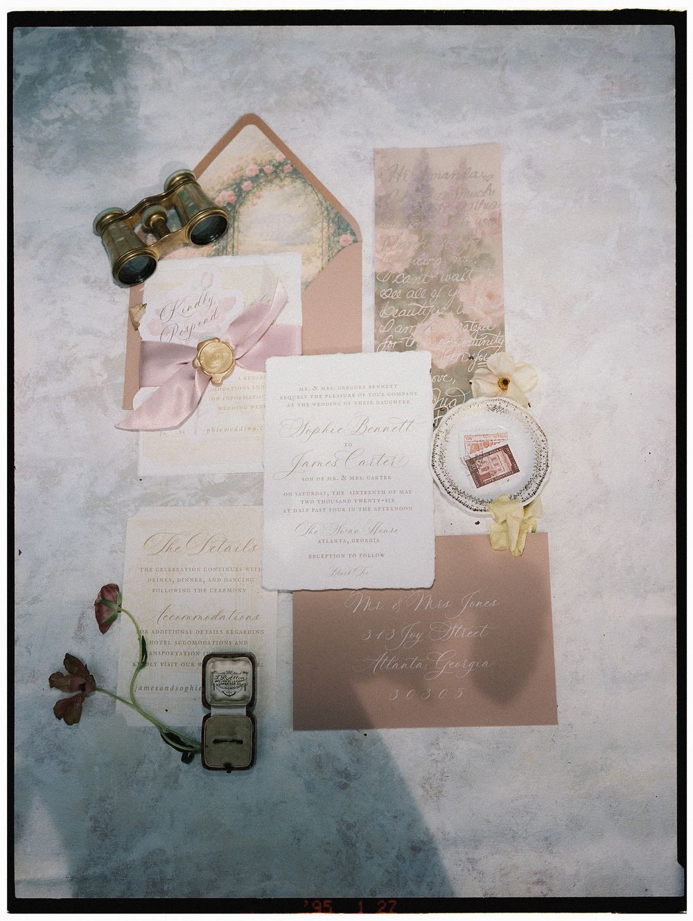 Elegant wedding invitation suite with blush pink envelopes, floral accents, calligraphy cards, vintage binoculars, and a ring box flatlay.