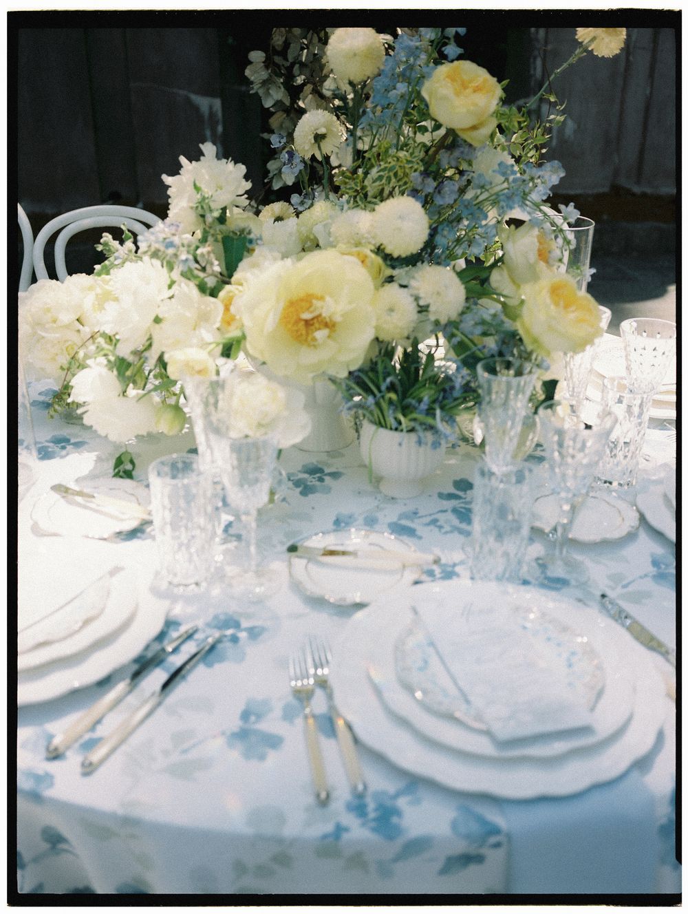 Elegant wedding tablescape with white and yellow floral centerpiece, crystal glasses, and blue floral linen.