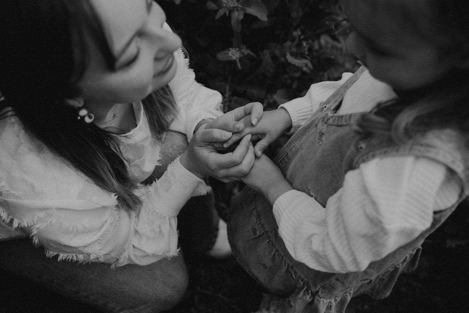 Black and white photo of two young girls holding hands together outdoors near leafy foliage.