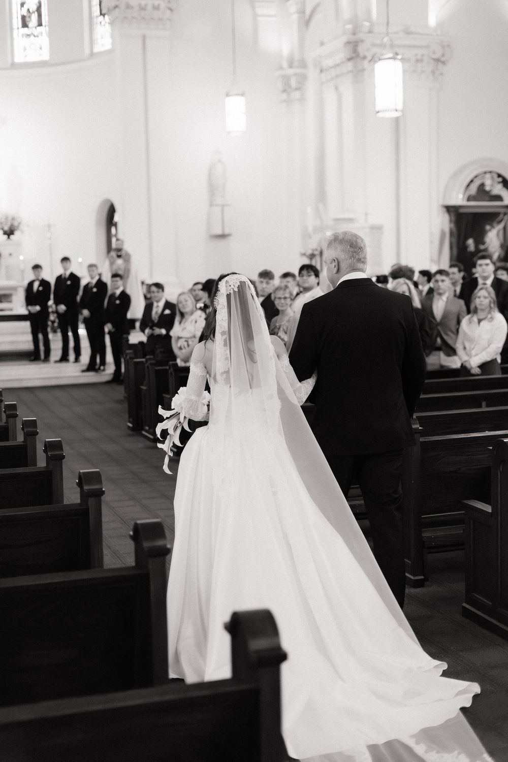 Black and white photo of a bride walking down the church aisle with her escort during a traditional wedding ceremony.