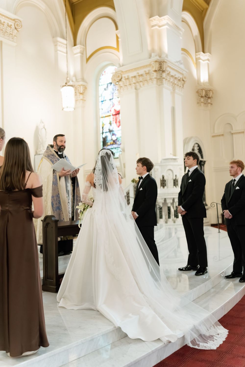 Bride and groom stand at the altar during a elegant church wedding ceremony with groomsmen and officiant.