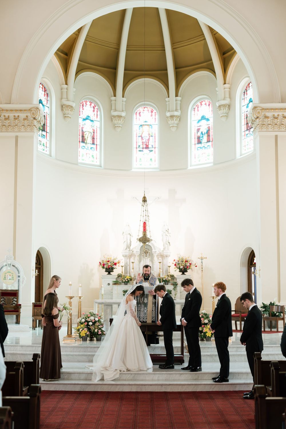 Bride and groom exchange vows at elegant church altar with stained glass windows and floral arrangements.