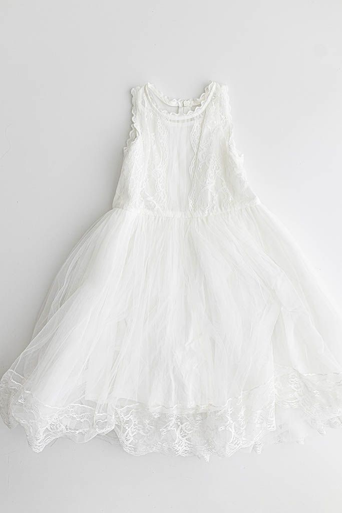 White sleeveless girls dress with lace bodice, tulle skirt layers and delicate floral embroidered hem, laid flat.