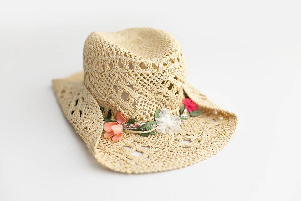 Natural straw crochet cowboy hat with floral band decoration, displayed on white background.