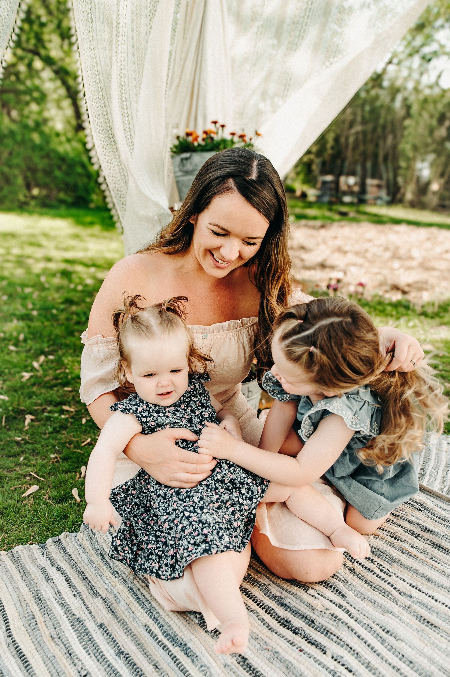 Family of six posing outdoors in a green field during golden hour, mother holding toddler surrounded by children.